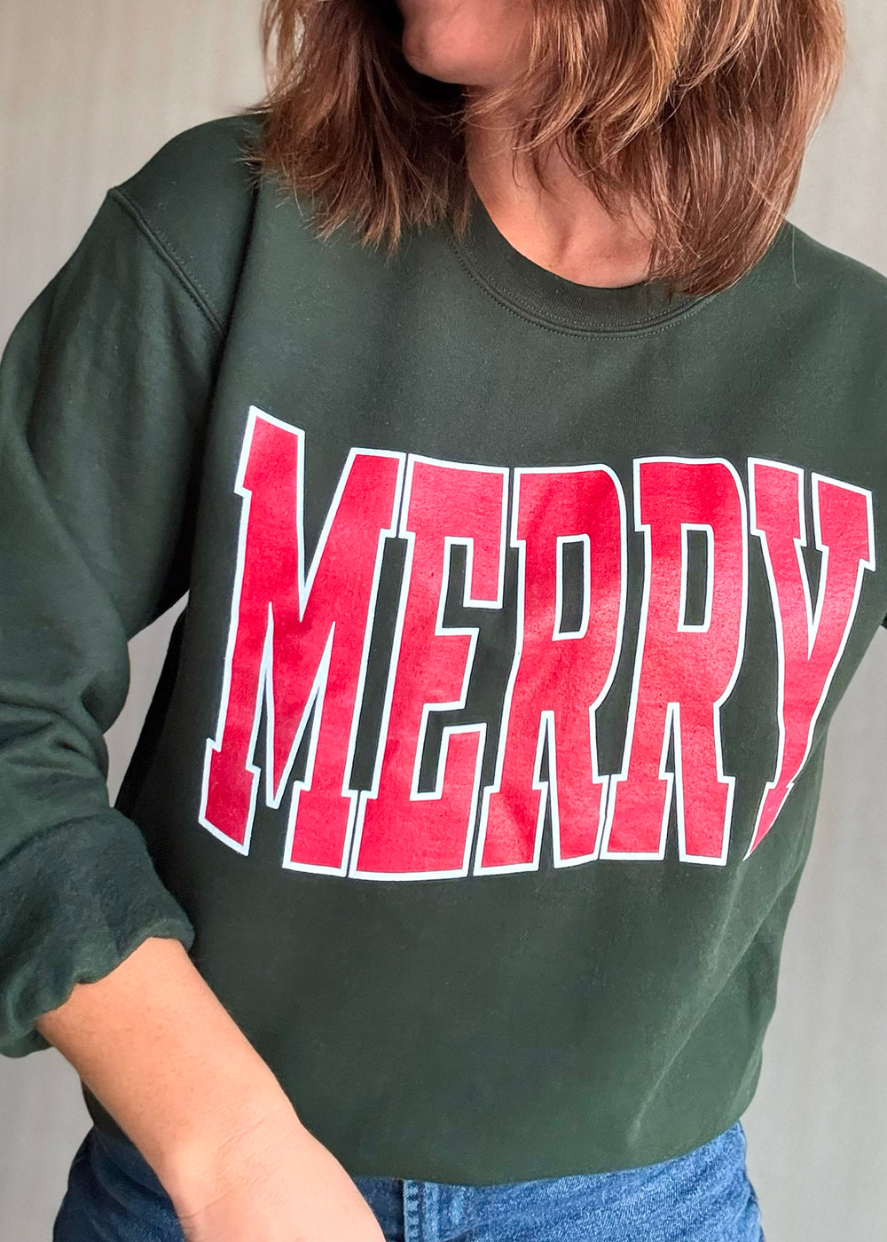 Person wearing a green sweatshirt with 'MERRY' in red letters on a plain background