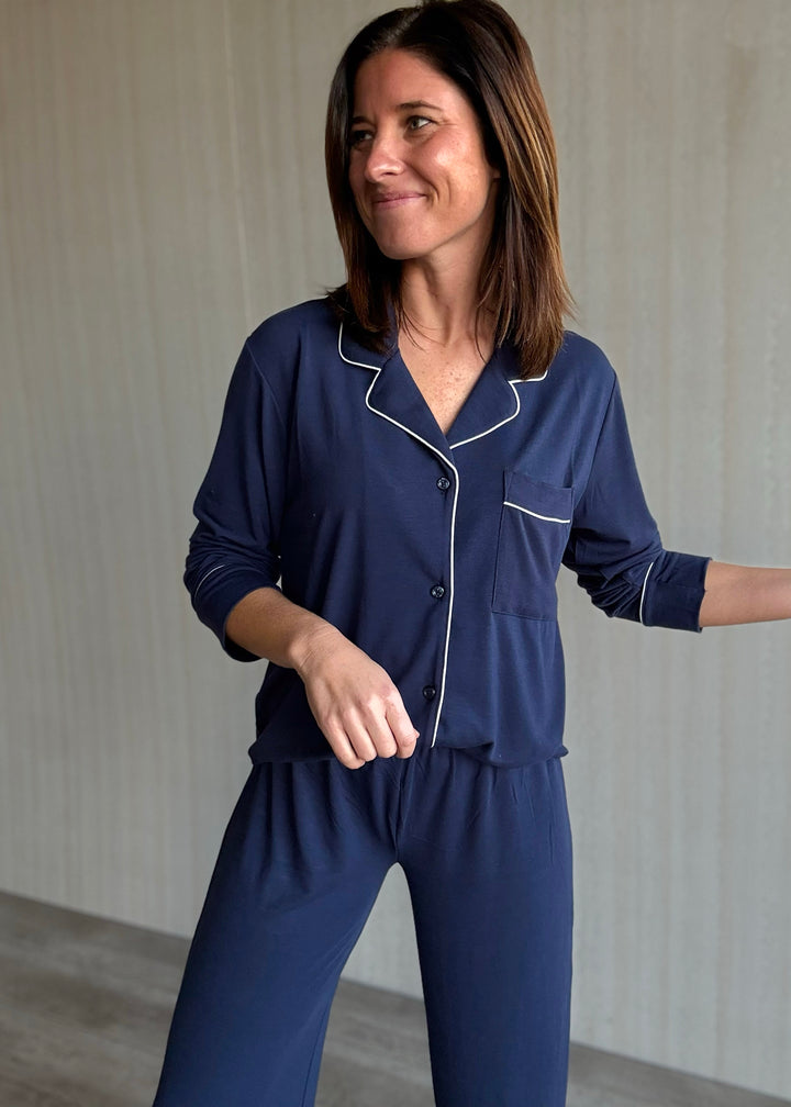 Woman wearing a navy blue pajama set with white piping against a neutral background