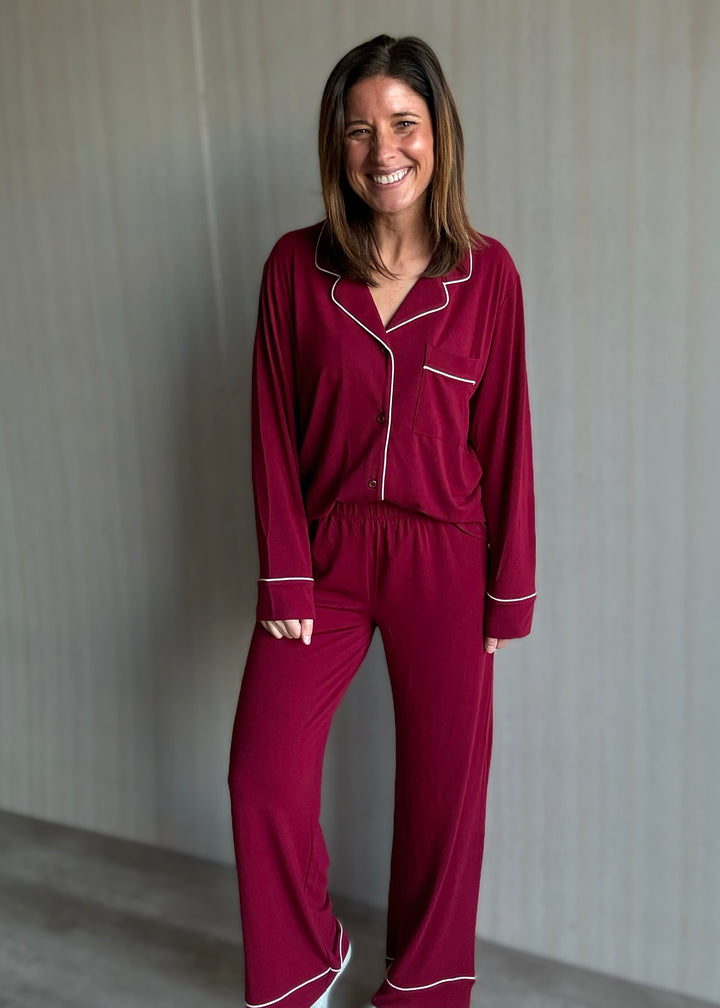 Woman wearing a burgundy pajama set with white piping against a neutral background