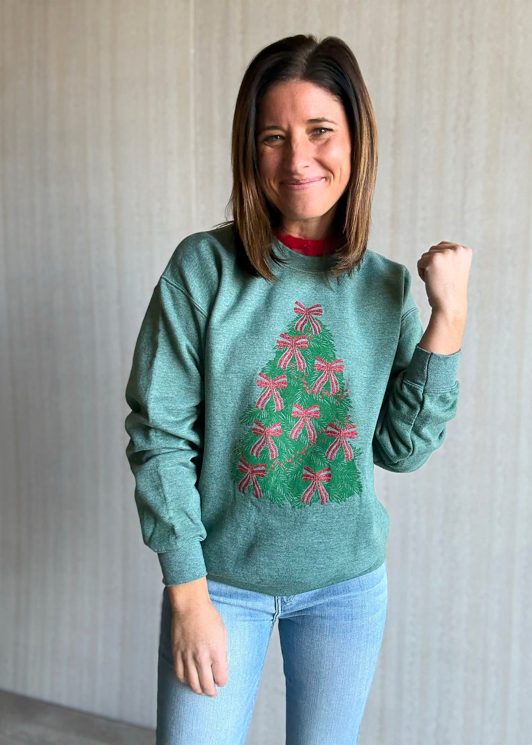 Woman wearing a green sweater with a Christmas tree design, standing against a plain background.