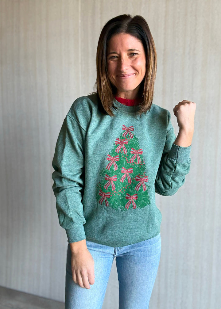 Woman wearing a green sweater with a Christmas tree design, standing against a plain background.