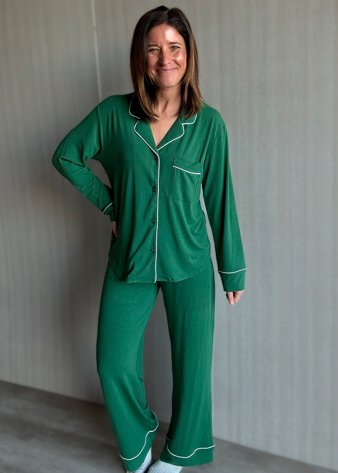Woman wearing a green pajama set with white piping against a neutral background