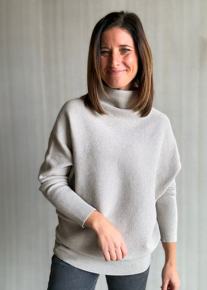 Woman wearing a light gray sweater against a plain background