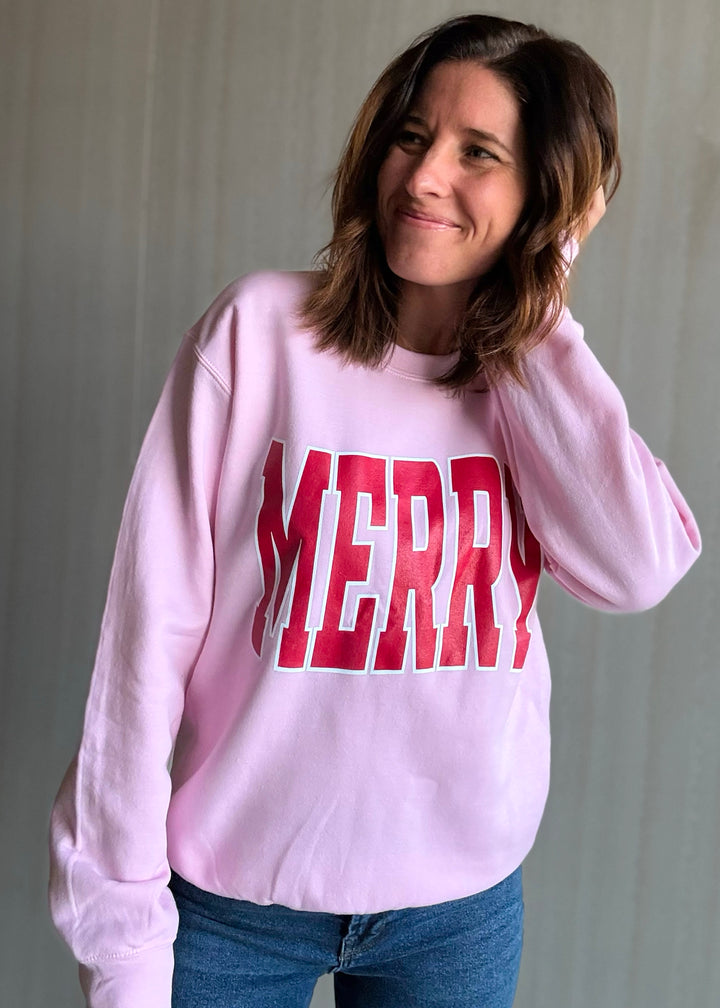 Person wearing a pink sweatshirt with 'MERRY' printed in red letters against a neutral background
