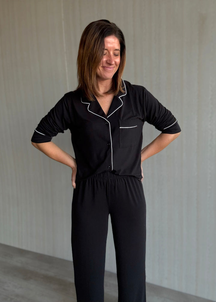 Woman wearing a black pajama set with white piping against a neutral background