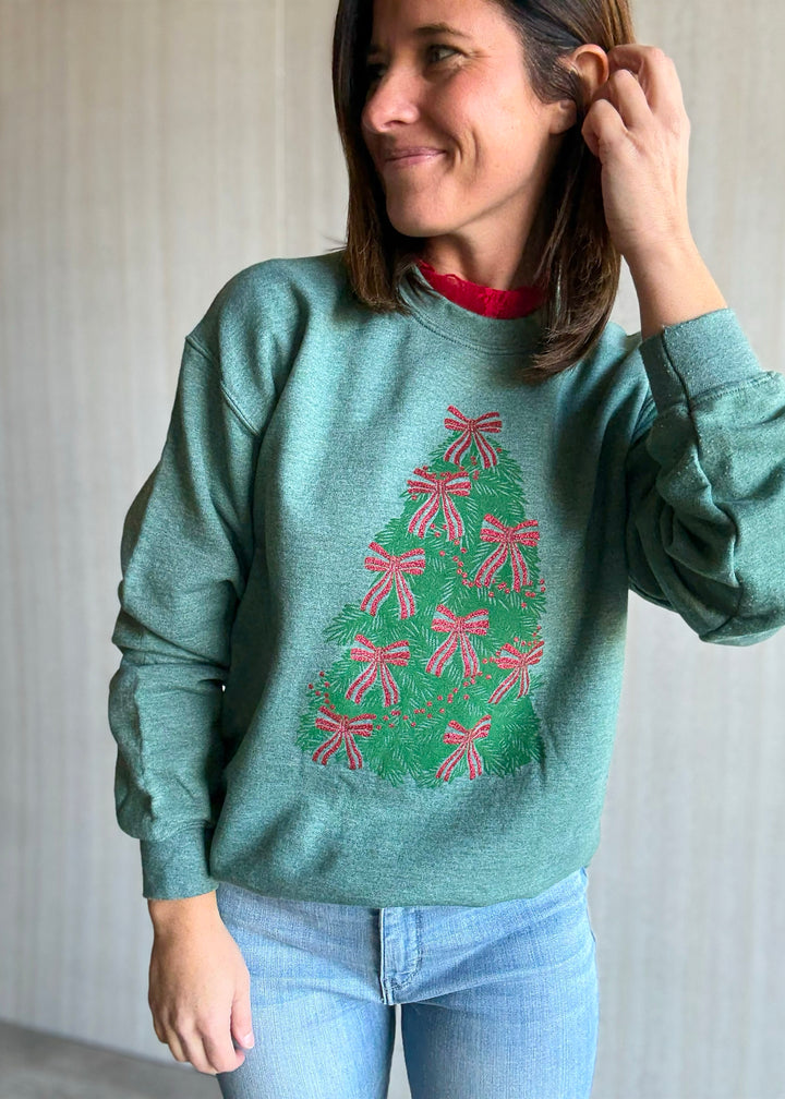 Woman wearing a green sweater with a Christmas tree design, standing against a plain background.