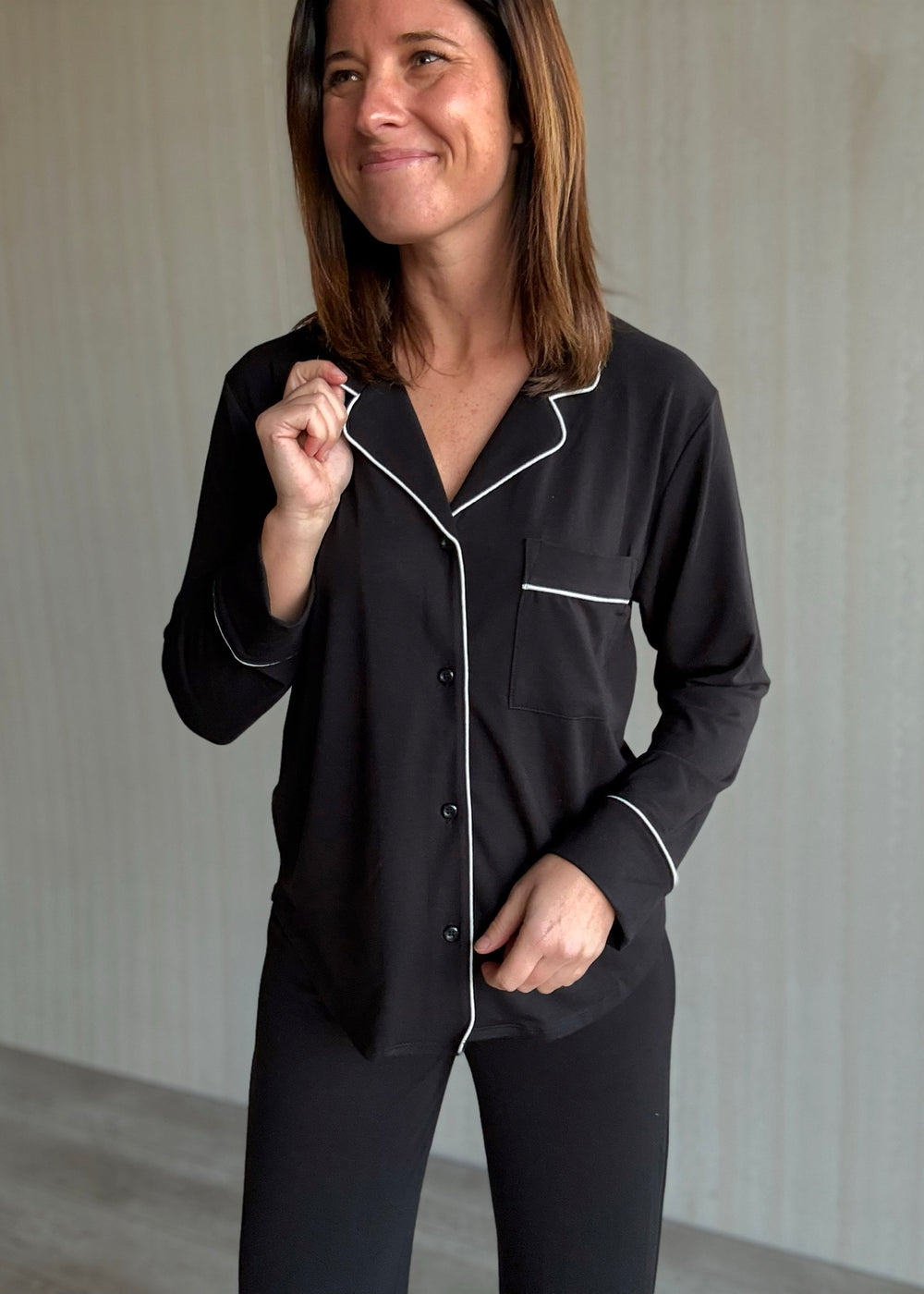Woman wearing black pajamas with white piping against a neutral background