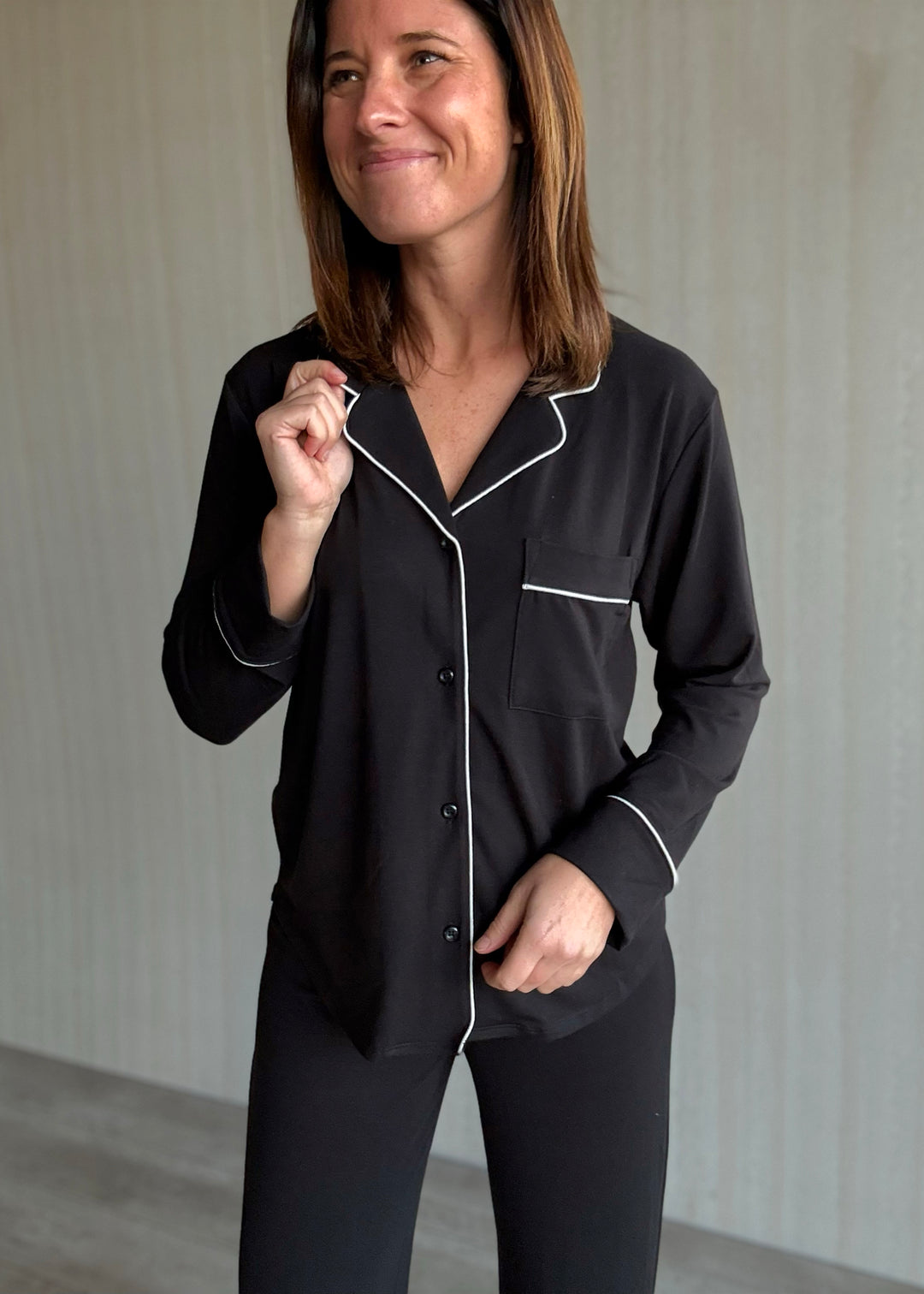 Woman wearing black pajamas with white piping against a neutral background