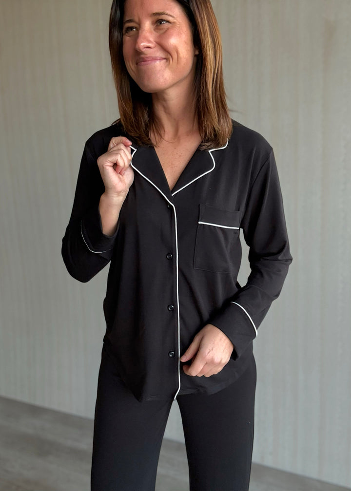 Woman wearing black pajamas with white piping against a neutral background