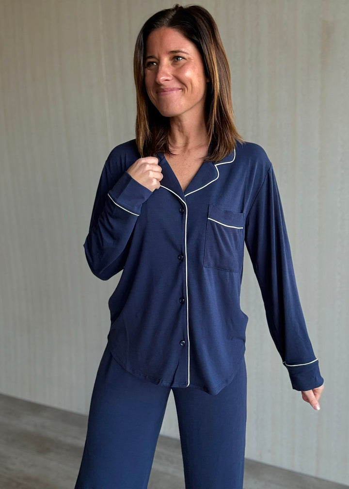 Woman wearing a navy blue pajama set with white piping against a neutral background