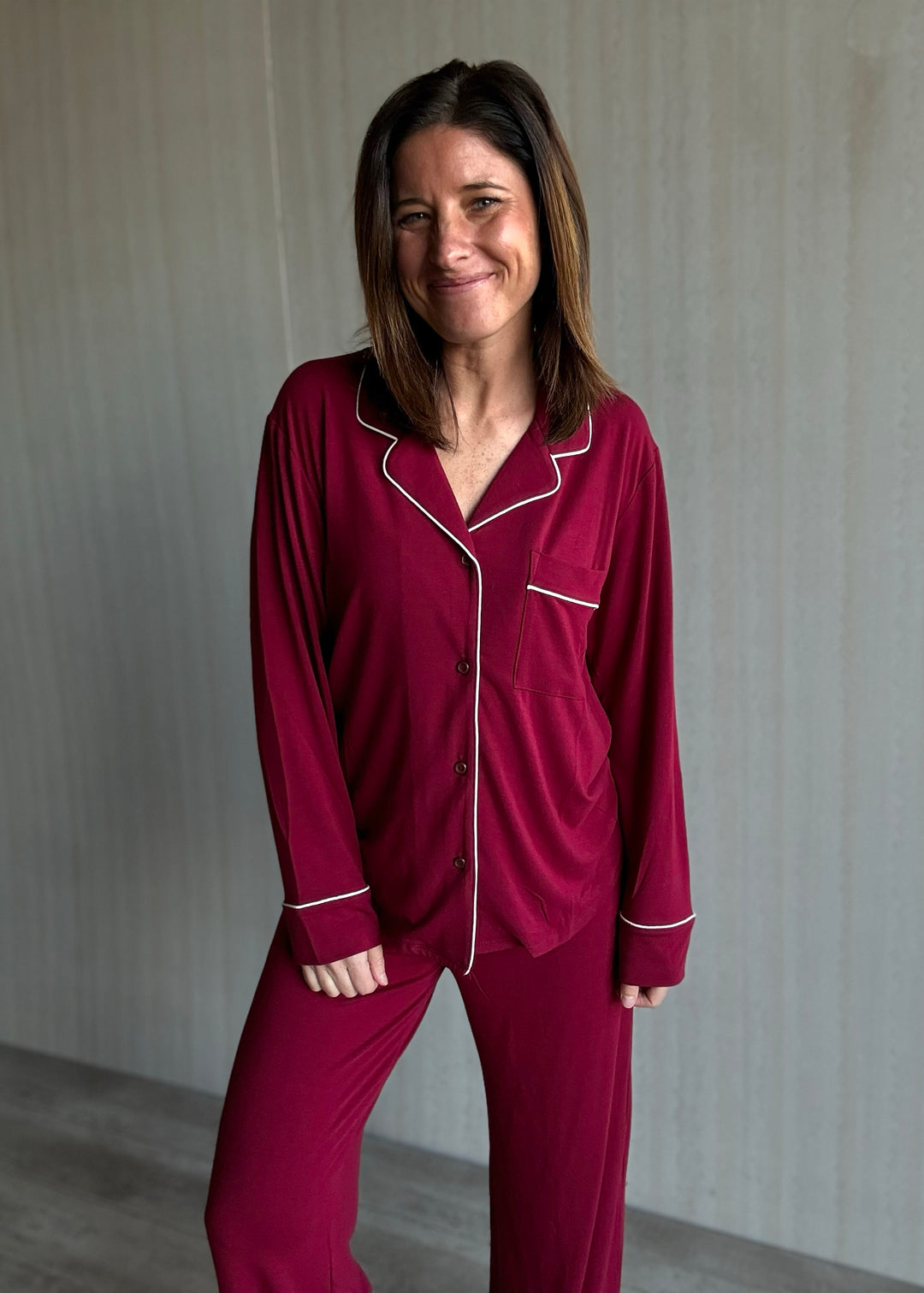 Woman wearing a burgundy pajama set with white piping against a plain background