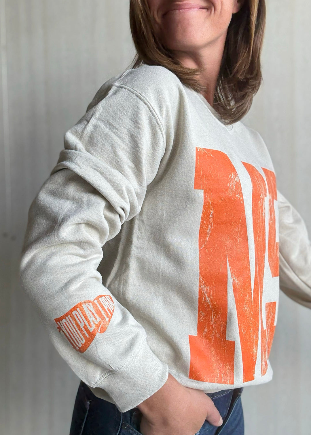 Person wearing a white sweatshirt with orange text and graphics | Women's Mahomet Seymour Cream and Orange Sweatshirt Fanwear
