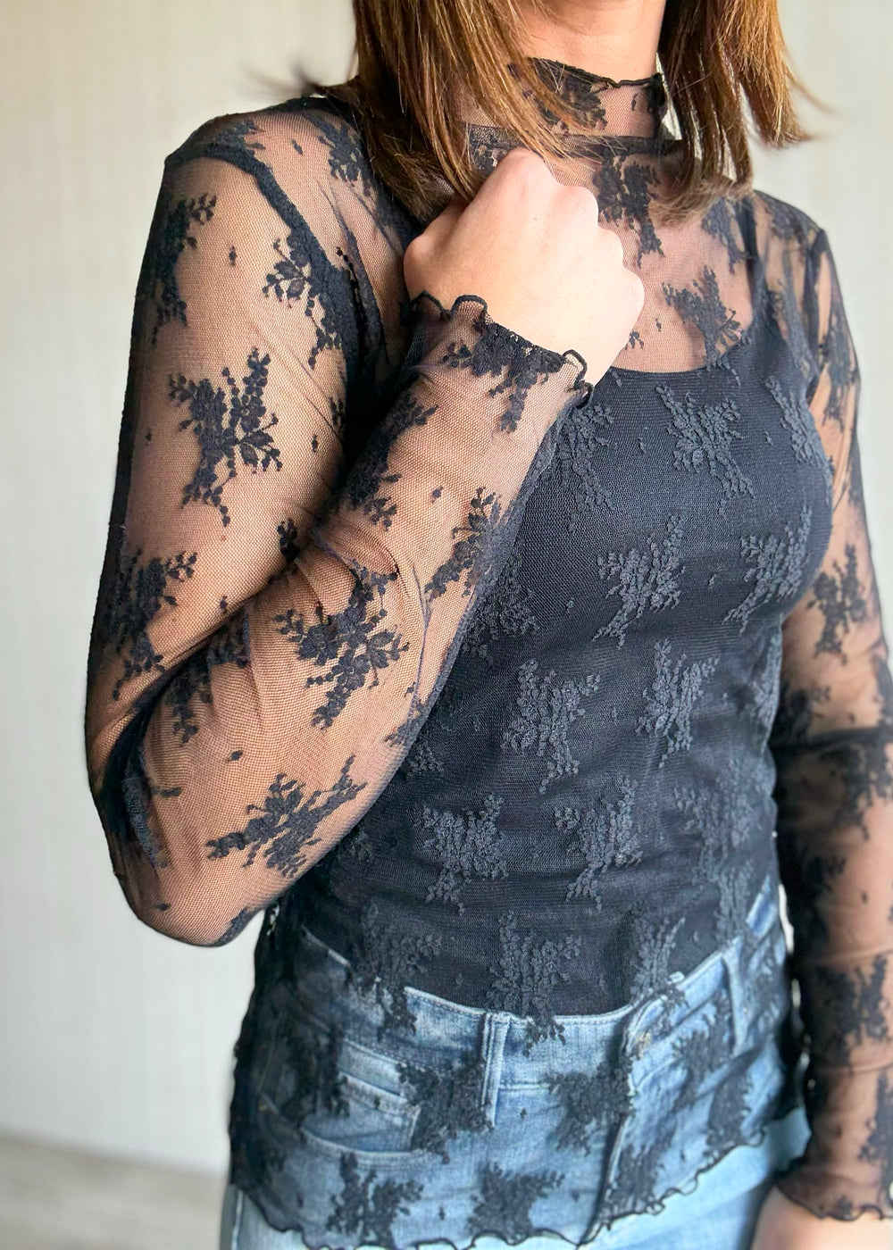 Woman wearing a black lace top and light blue jeans against a neutral background. Women's Long-Sleeve Black Lace Sheer Layering Top.