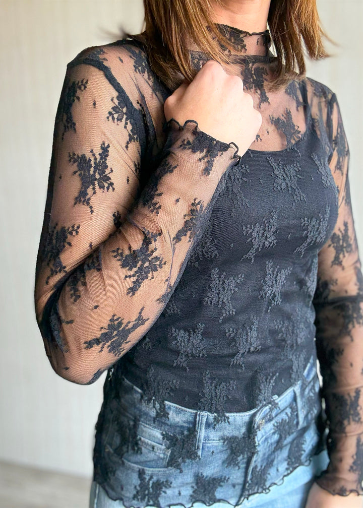 Woman wearing a black lace top and light blue jeans against a neutral background. Women's Long-Sleeve Black Lace Sheer Layering Top.