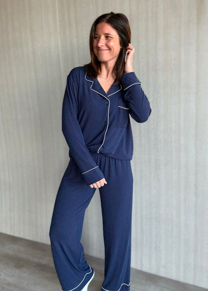Woman wearing a navy blue pajama set with white piping against a neutral background