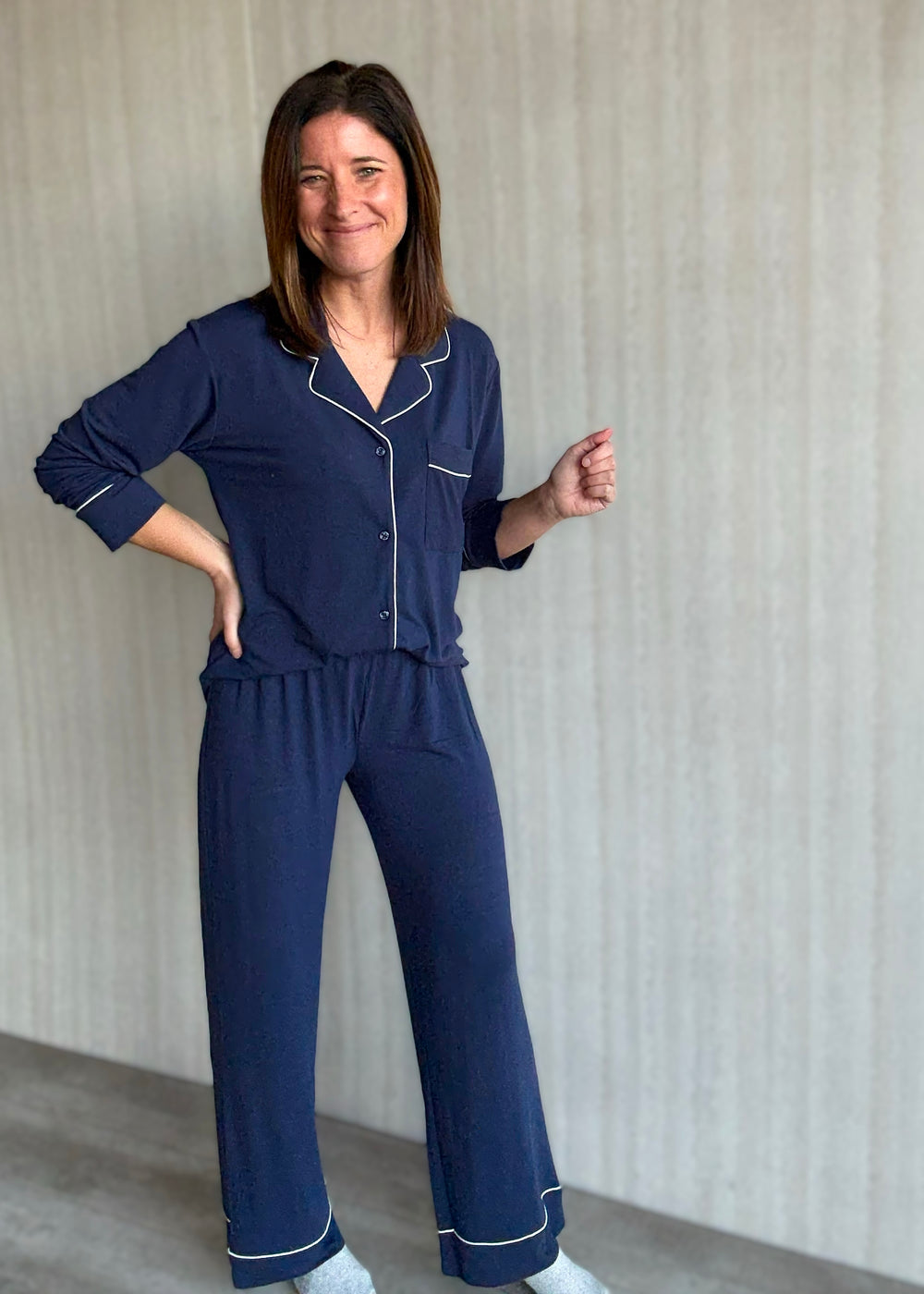 Woman wearing a navy blue pajama set with white piping against a neutral background