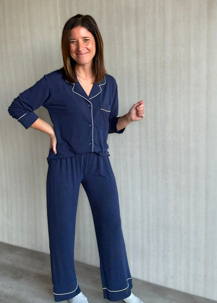 Woman wearing a navy blue pajama set with white piping against a neutral background