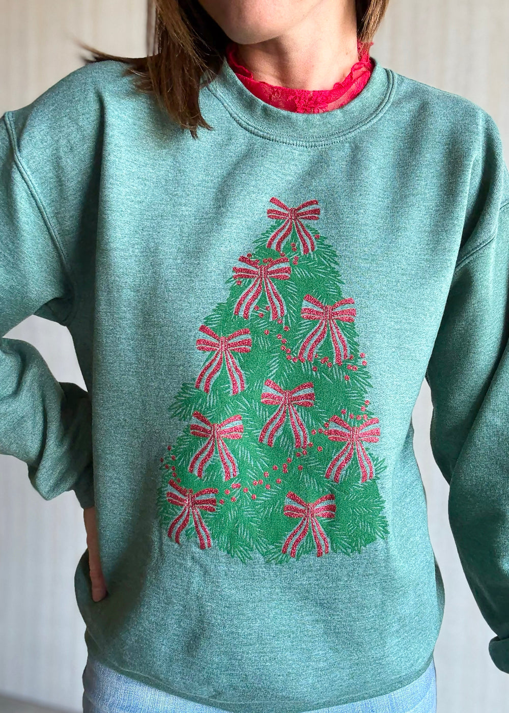 Person wearing a green sweatshirt with a Christmas tree design featuring red bows.