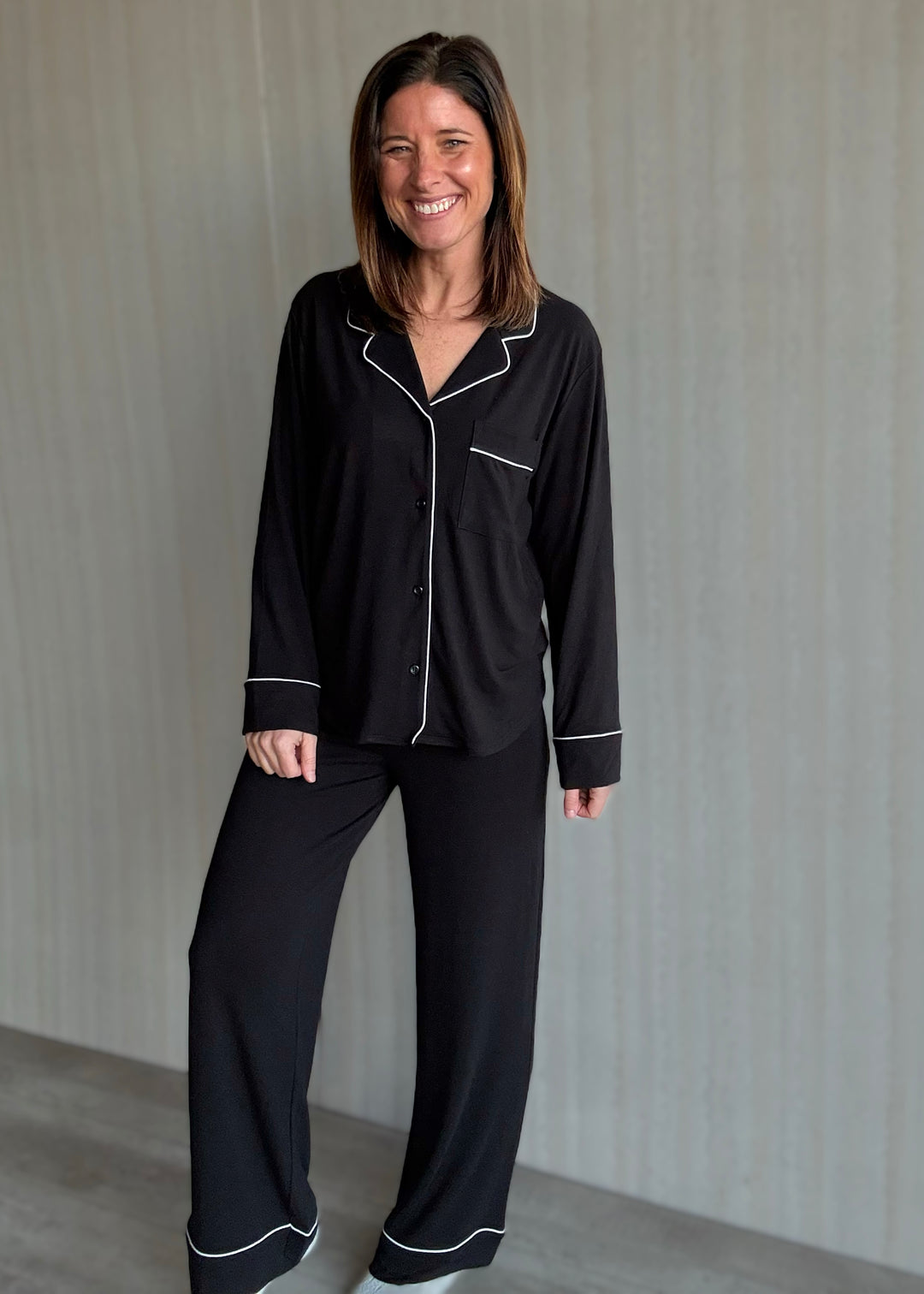 Woman wearing black pajamas with white piping against a neutral background