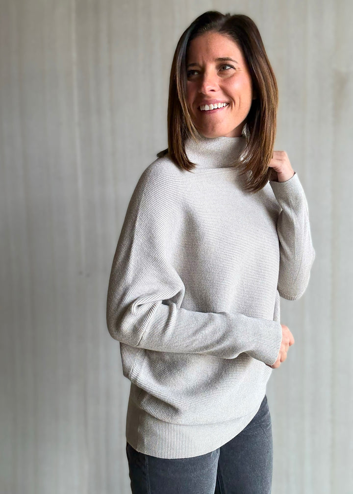 Woman wearing a light gray turtleneck sweater against a plain background