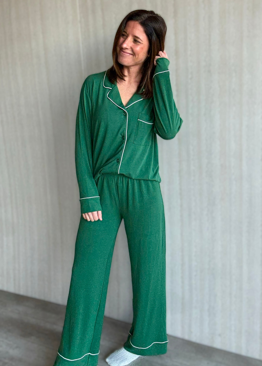 Woman wearing a green pajama set with white piping against a neutral background