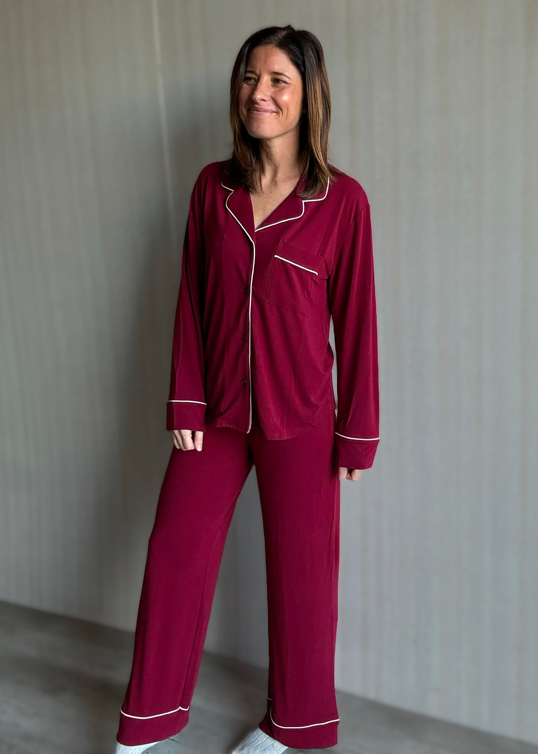 Woman wearing a burgundy pajama set with white piping against a plain background