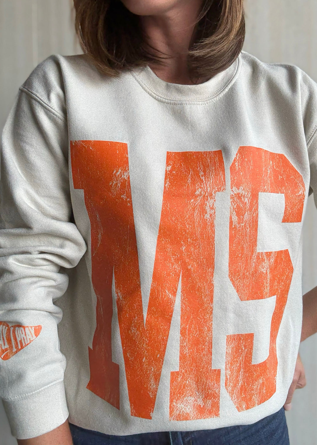 Person wearing a white sweatshirt with orange text and graphics | Women's Mahomet Seymour Cream and Orange Sweatshirt Fanwear