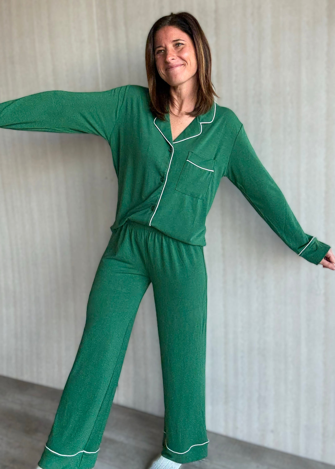 Woman wearing a green pajama set with white piping against a neutral background