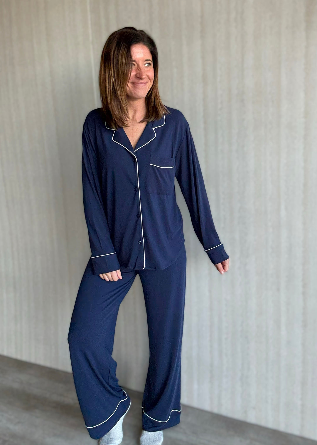 Woman wearing a navy blue pajama set with white piping against a neutral background