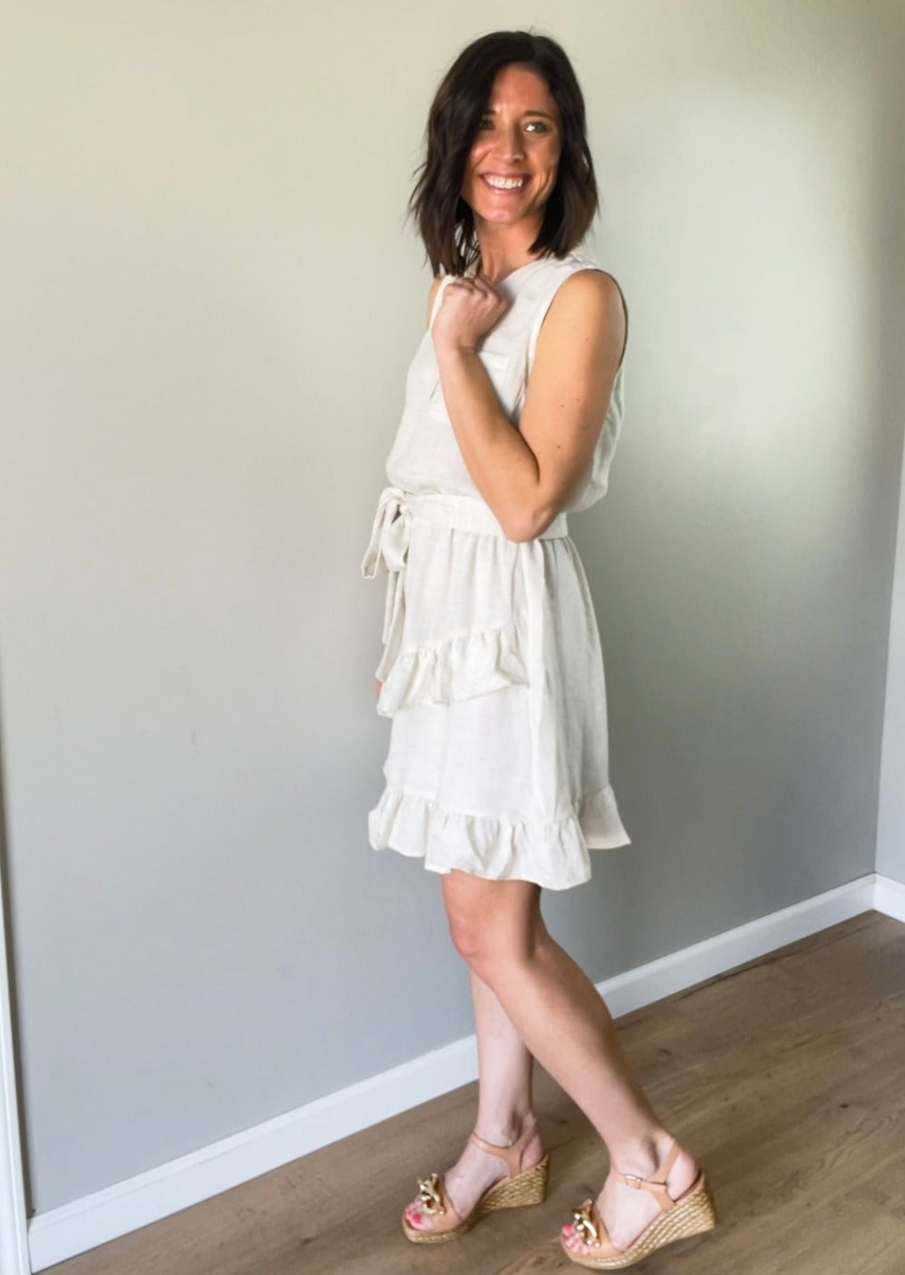 Light cream linen summer sleeveless dress with ruffle skirt and tie belt.