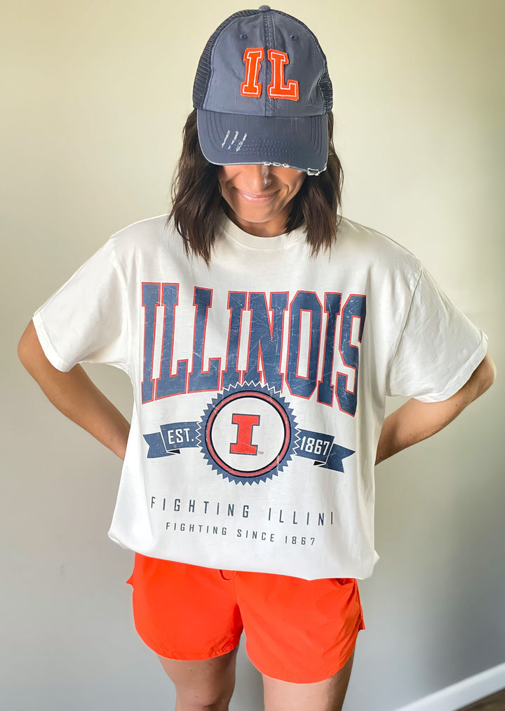 This Illinois Ivory Oversized Tee features an oversized fit just as the title says. Text graphics state "ILLINOIS" across the top chest in a light blue distressed lettering with an orange outline followed by an Illinois emblem with "Est. 1867". "FIGHTING ILLINI | FIGHTING SINCE 1867" stated across the bottom of the shirt and light blue. The short sleeves and crew neck add a classic touch, making it easy to wear with a variety of outfits.